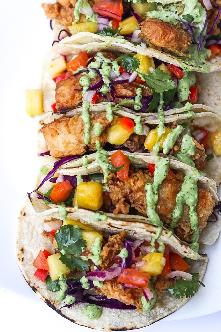 Crispy golden fish tacos served in warm tortillas and topped with creamy cilantro lime sauce, fresh cabbage, avocado, and colorful peppers for a bold and flavorful taco night meal.
