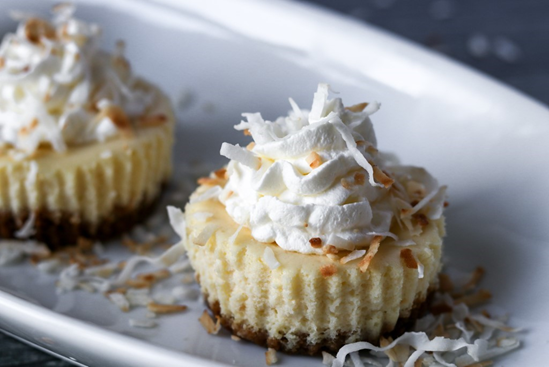 mini coconut pineapple rum cheesecakes topped with toasted coconut and whipped cream in a muffin pan