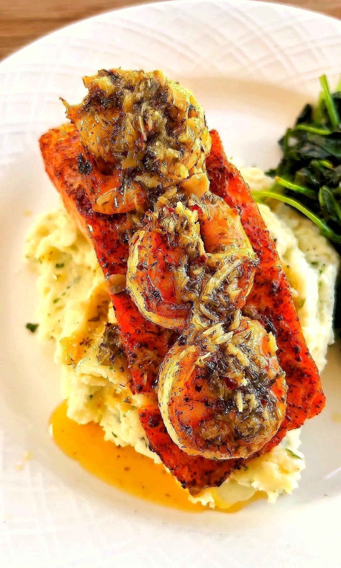 Blackened salmon and shrimp served with creamy garlic herb mashed potatoes and sautéed spinach on a white plate